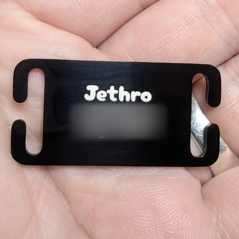 Small black Silent Slide-On dog tag engraved Jethro, held in a hand, with the phone number blurred